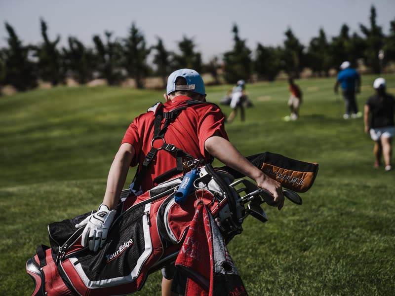 Golfer carrying a bag across a course with players behind